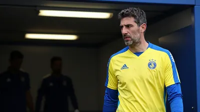A 35-year-old, ruggedly-built goalkeeper, dressed in a plain yellow and blue polyester training top, stands in the...