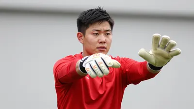 A tight shot of a 28-year-old goalkeeper in a red jersey, mid-save with gloves outstretched