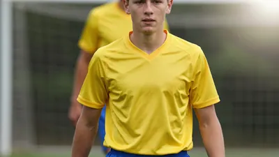 A photorealistic image of a young, anonymous winger, aged 16-18, wearing a yellow jersey with a smooth, unbroken fabric...