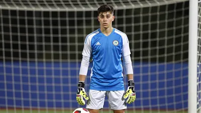 A 20-year-old goalkeeper in a UD Las Palmas jersey, with a determined expression, standing in front of a goal, with a...
