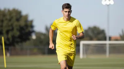 A 28-year-old athletic centre-back in a solid yellow jersey, mid-stride on a sunlit training pitch