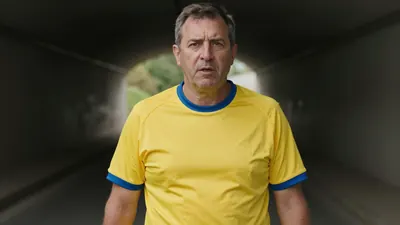 Middle-aged male club official, athletic build, waist-up, wearing a plain yellow shirt with blue trim, smooth cotton...