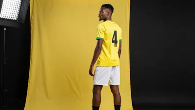 A tight waist-up shot of a 29-year-old Ghanaian center-back in a yellow jersey with a black number 4 on the back, wearing...