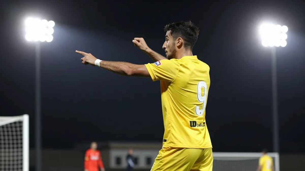 A tight waist-up shot of a UD Las Palmas player in a yellow jersey with a white number on the back, looking determined as...