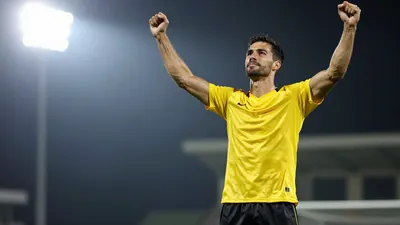 A muscular 25-30 year old male football player in a solid yellow jersey and black shorts, celebrating with arms raised
